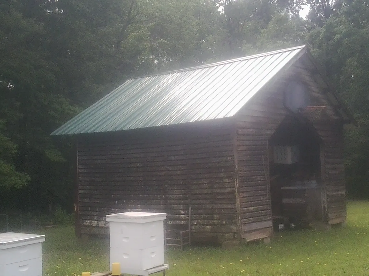 Green metal roof on a weathered barn beside stacked beehives in Summit