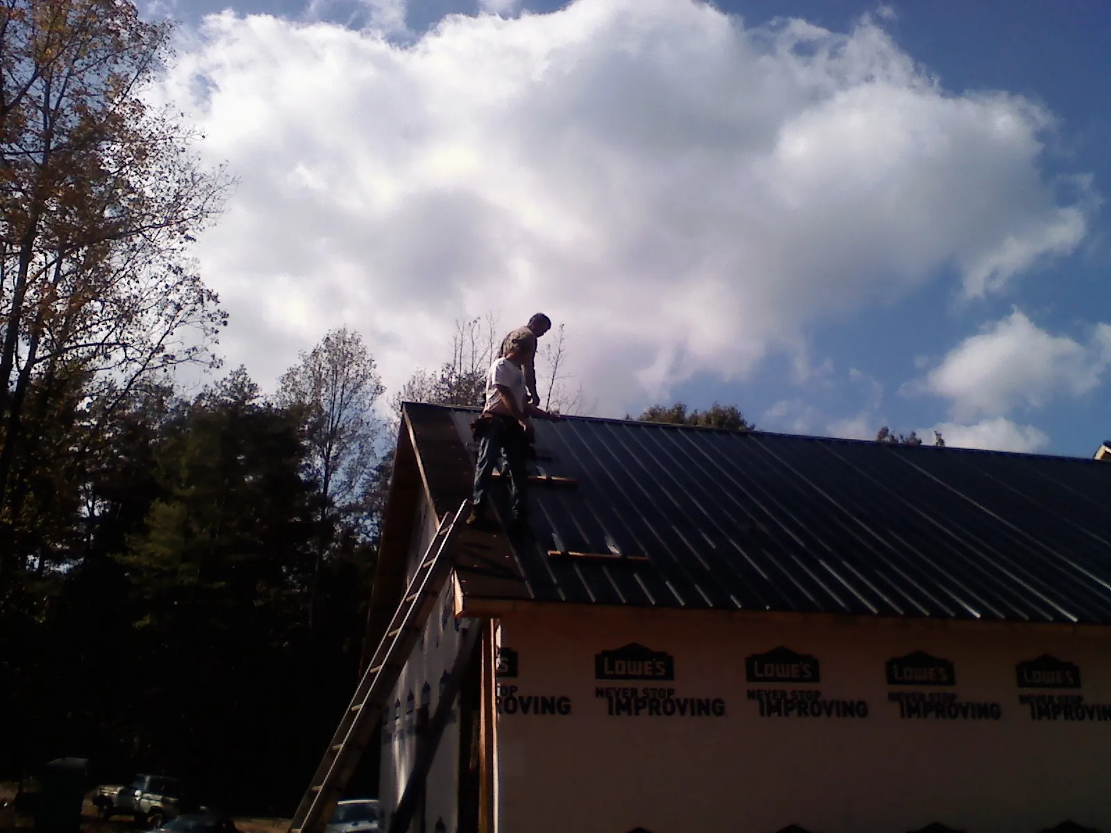 Roofer fastening dark metal panels high against a cloudy sky, from a Roof Inspection job in Summit